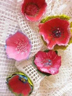 three red flowers sitting on top of a white table cloth next to two green and pink flowers