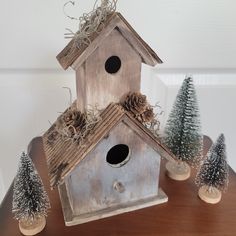 a bird house with pine cones on the roof and two small trees next to it