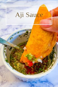 a hand holding a piece of food over a bowl filled with soup and sauces