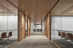 an empty office with glass walls and wooden chairs on either side of the desks