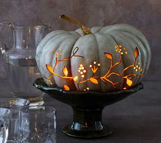 a white pumpkin decorated with leaves and flowers on a black plate next to silverware