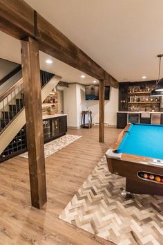 a pool table in the middle of a living room with stairs leading up to it