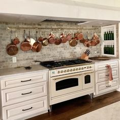 a stove top oven sitting inside of a kitchen under hanging pots and pans on the wall