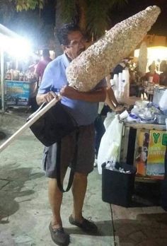 a man holding a large loaf of bread on top of a wooden stick in his hand