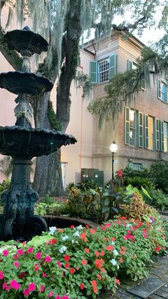 a fountain surrounded by flowers in front of a building