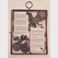 an open book with flowers and leaves on it hanging from the wall next to a frame