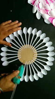 someone is making a paper fan out of white plastic spoons and some glue on the table