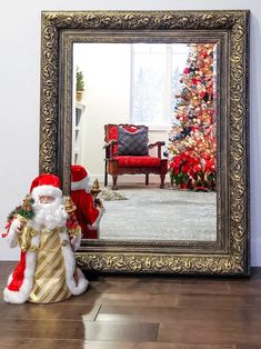 a santa clause standing next to a christmas tree in front of a large framed mirror