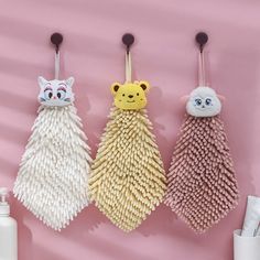 three toothbrush holders hanging on a pink wall with two cats and one cat in the middle