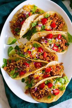 three tacos on a plate with lettuce, tomatoes and other toppings