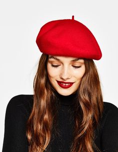 a woman wearing a red beret with long hair and lipstick on her lips is looking down at the camera