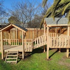 a wooden play set in the grass next to a tree and fenced area with trees