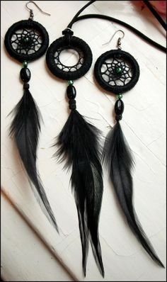 three black dream catchers with feathers hanging from it's earring wires on a white surface