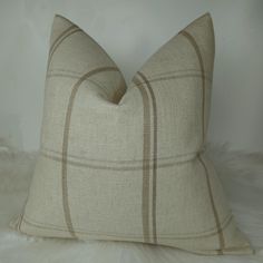 a white and brown plaid pillow sitting on top of a furnishing floor next to a wall