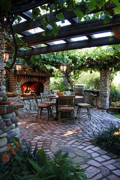 an outdoor dining area with stone fireplace and table surrounded by greenery on either side