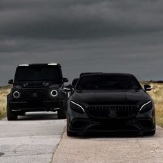 two black mercedes benz vehicles parked on the side of the road with dark clouds in the background