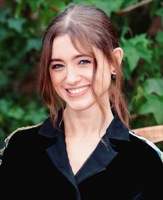 a smiling woman with long hair wearing a black shirt and green leaves in the background