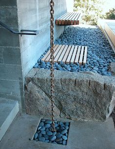 a bench sitting on top of a cement slab next to a stone wall and water feature