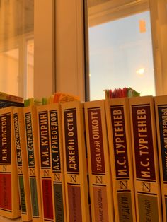 a row of books sitting on top of a table next to a window sill