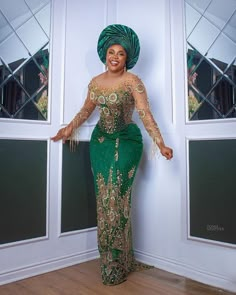 a woman in a green and gold dress standing next to a wall with her hands on her hips