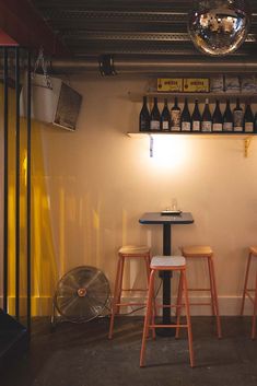 two stools and a table in a room with wine bottles on the wall behind them