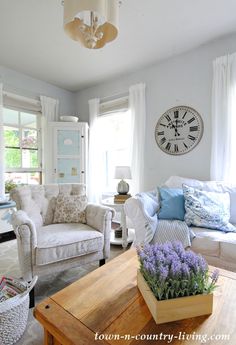 a living room filled with furniture and a clock on the wall above it's windows