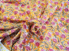 an orange and pink flowered fabric with green leaves on it, next to a pair of scissors