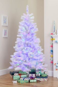 a white christmas tree with colorful lights and presents on the floor in front of it