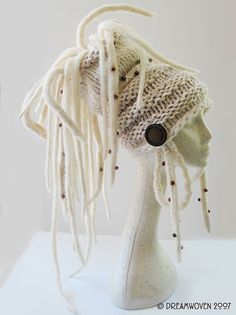 a white mannequin head wearing a knitted hat with fringes and buttons