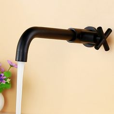 a black faucet with water running from it's spout and flowers in the background