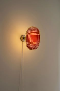 a red and yellow lamp on a white wall next to a light fixture with a long cord