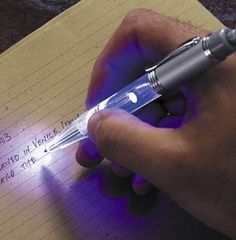 a person holding a pen and writing on a piece of paper with purple light coming from it