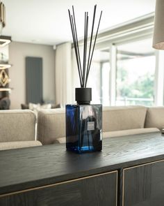 a blue glass bottle with reeds in it sitting on a wooden table next to a couch