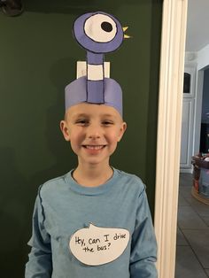 a young boy wearing a paper hat that says hey can i drive the bus?