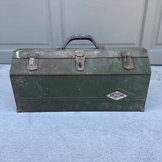 an old green metal tool box sitting in front of a garage door with the lid open