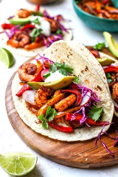 two shrimp tacos with red cabbage and avocado on a wooden cutting board