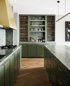 a kitchen with green cabinets and marble counter tops, gold hoods over the stove