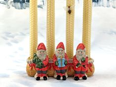 two santa claus figurines sitting next to some candles in the snow