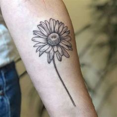 a black and white photo of a flower tattoo on the left arm, with a single daisy in the center