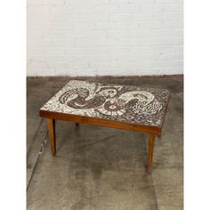 a coffee table with an intricately designed tile on the top and bottom, in front of a white brick wall