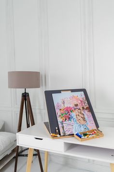 an easel is sitting on top of a white table with a painting and pencils