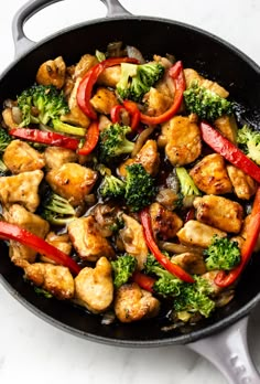 a skillet filled with chicken, broccoli and peppers on top of a white counter