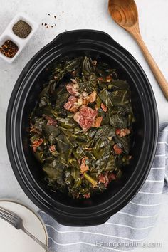 cooked collard greens in a slow cooker with wooden spoons and seasonings