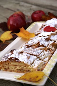 an apple pie with powdered sugar on top sits on a plate next to autumn leaves