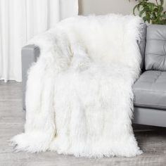 a couch with a white fluffy blanket on it's back next to a potted plant