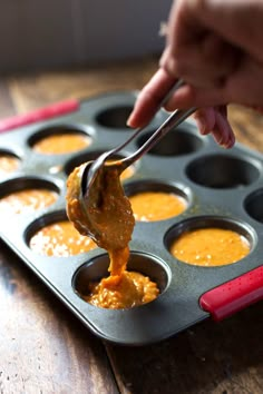 a person dipping sauce into a muffin tin