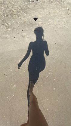 the shadow of a person holding a frisbee in front of their face on the beach