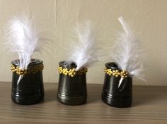 three black vases with white feathers in them