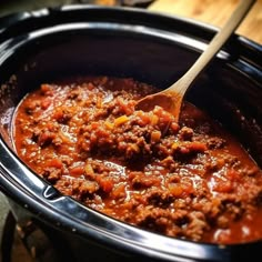 a wooden spoon is in a slow cooker filled with chili and meat stew, ready to be eaten