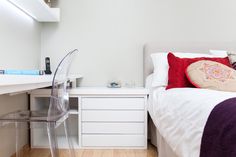 a white bed sitting next to a desk with a computer monitor on top of it